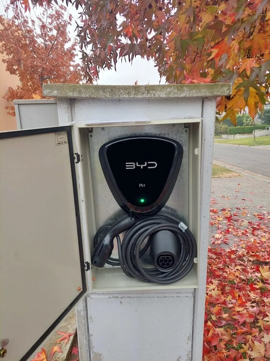 Cargador de auto eléctrico montado dentro de un gabinete en un pilar de entrada, con el cable enrollado